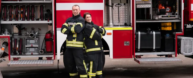 bombero hombre y mujer parados de frente a un camión de bomberos