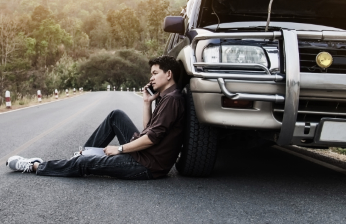 Persona sentada a un costado del vehiculo solicitando asistencia